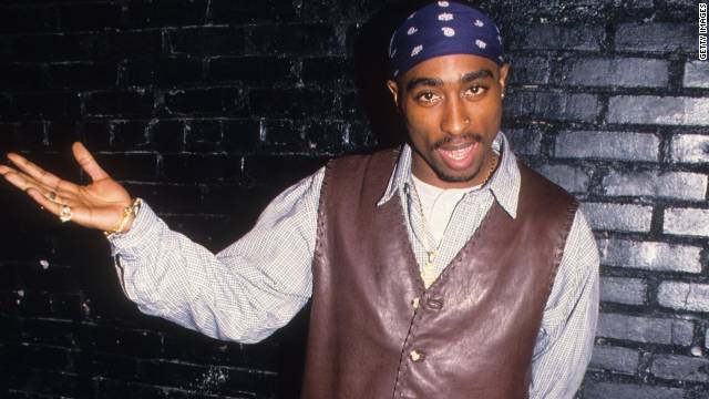 A black man putting on brown leather and white shirt and a blue badana